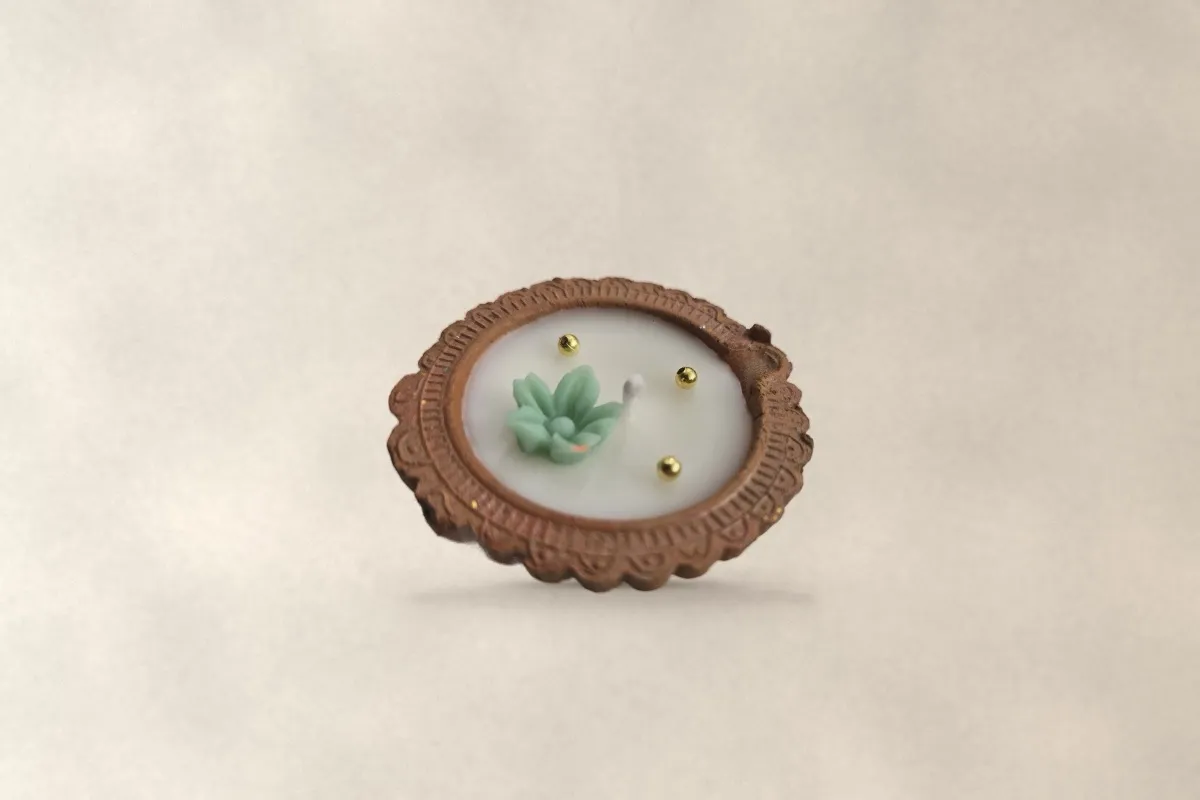 A terracotta diya filled with ivory wax and a mint wax flower